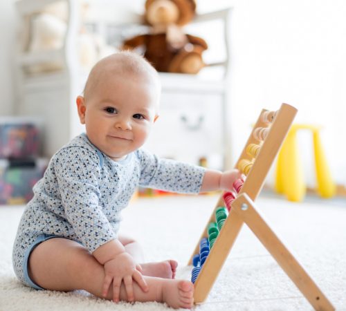 Cute little baby boy, playing with abacus at home, sunny kids room