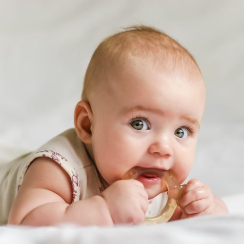 Six-month baby girl on her stomach with teether in the mouth